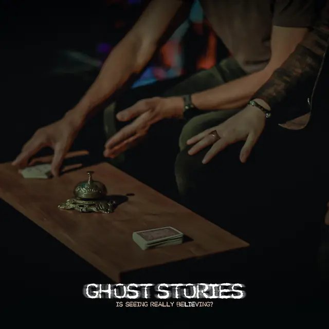 Hands hovering over a wooden table with a brass bell and a deck of cards