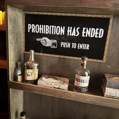 A "Prohibition Has Ended, Push to Enter" sign above a shelf of bottles