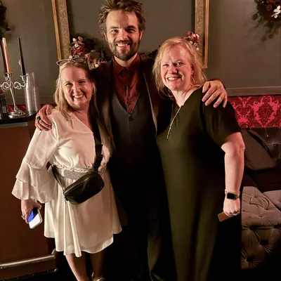 Two guests posing with Kent Axell in the speakeasy